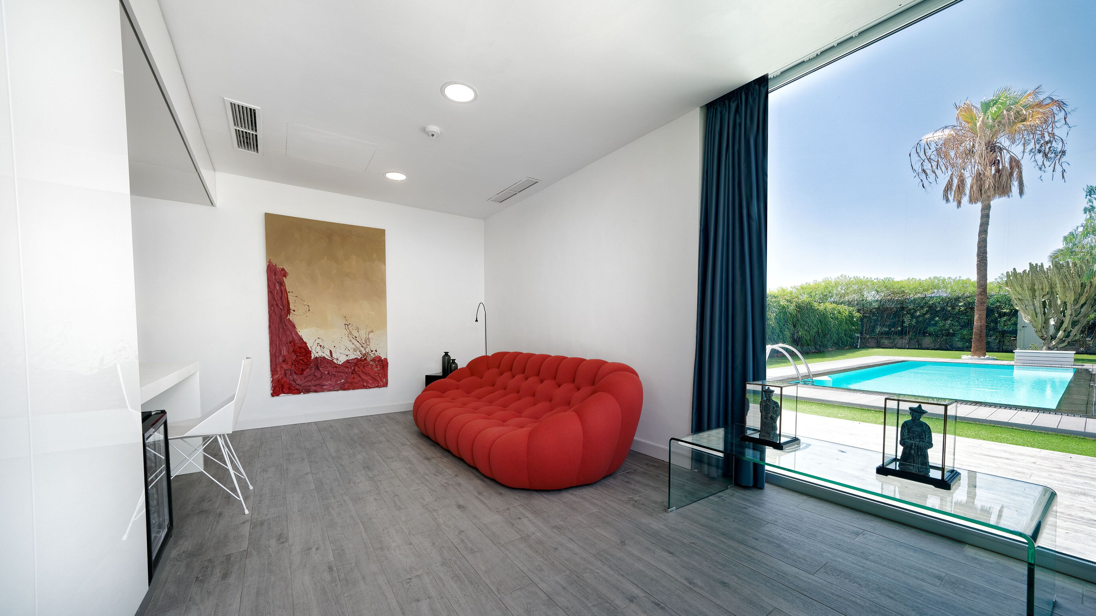Un salón moderno con un sillón de peluche rojo, un cuadro abstracto grande y vistas a una piscina.