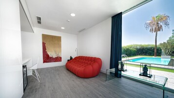 Un salón moderno con un sillón de peluche rojo, un cuadro abstracto grande y vistas a una piscina.