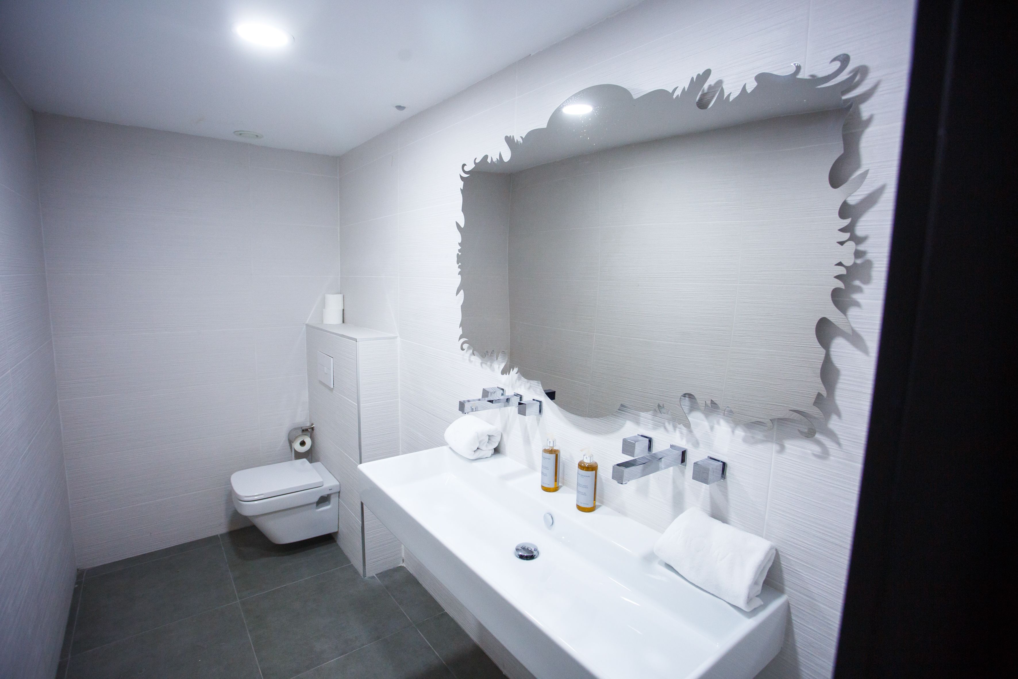 Un baño moderno con lavamanos, espejo y retrete blancos.