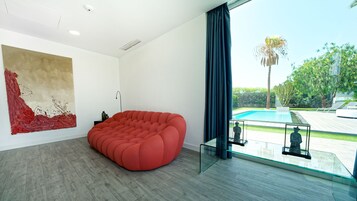 A modern living room with a red bean bag chair, a large abstract painting, and a view of a swimming pool.