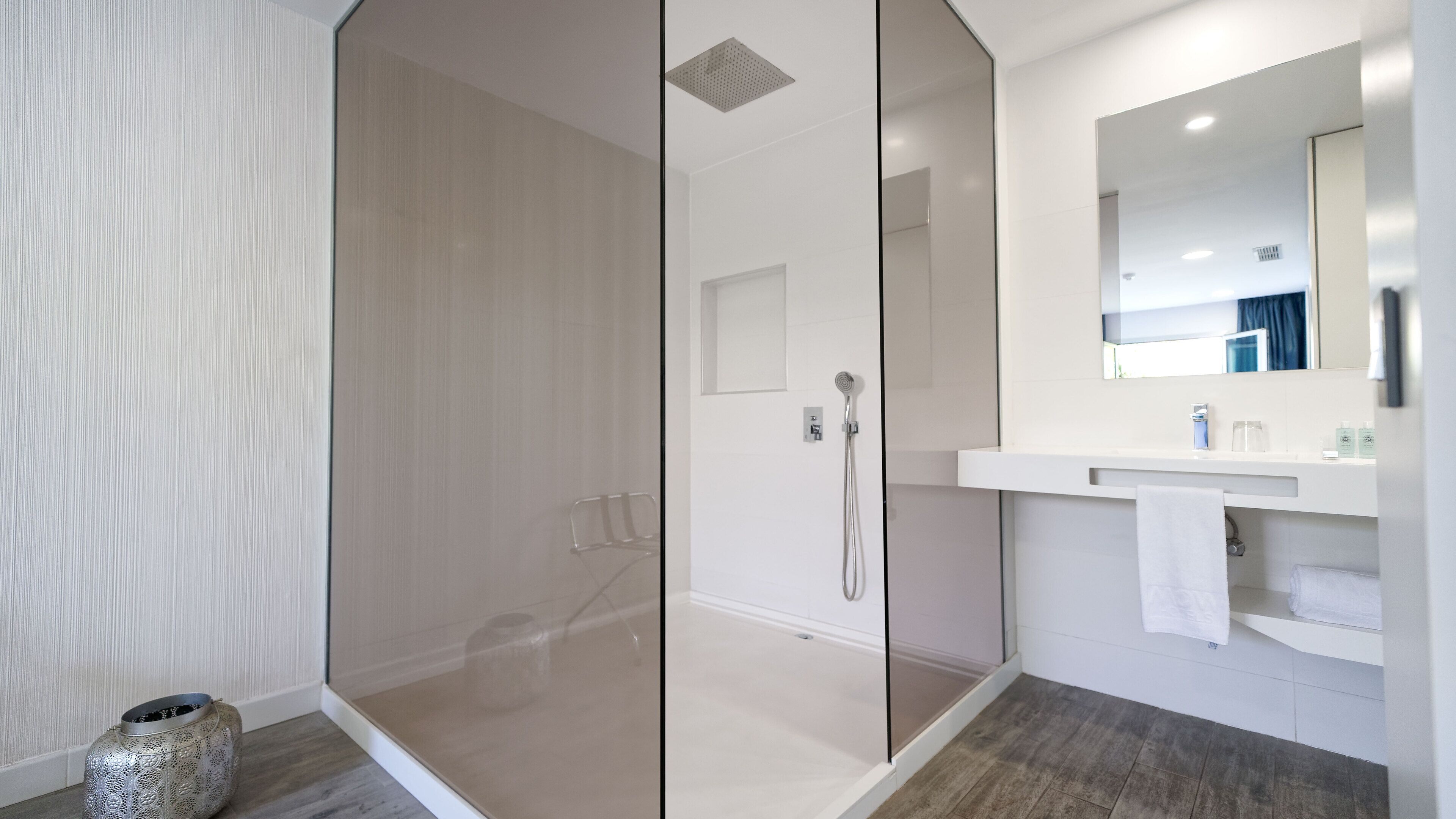A modern bathroom with a glass-enclosed shower, a white sink with a mirror, and a wooden floor.