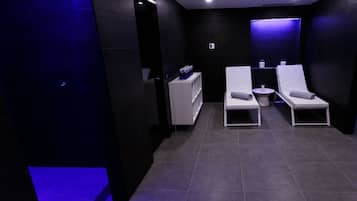Une salle de spa moderne équipée de deux fauteuils inclinables, d’une petite table blanche avec une serviette et d’une étagère contenant des bouteilles.