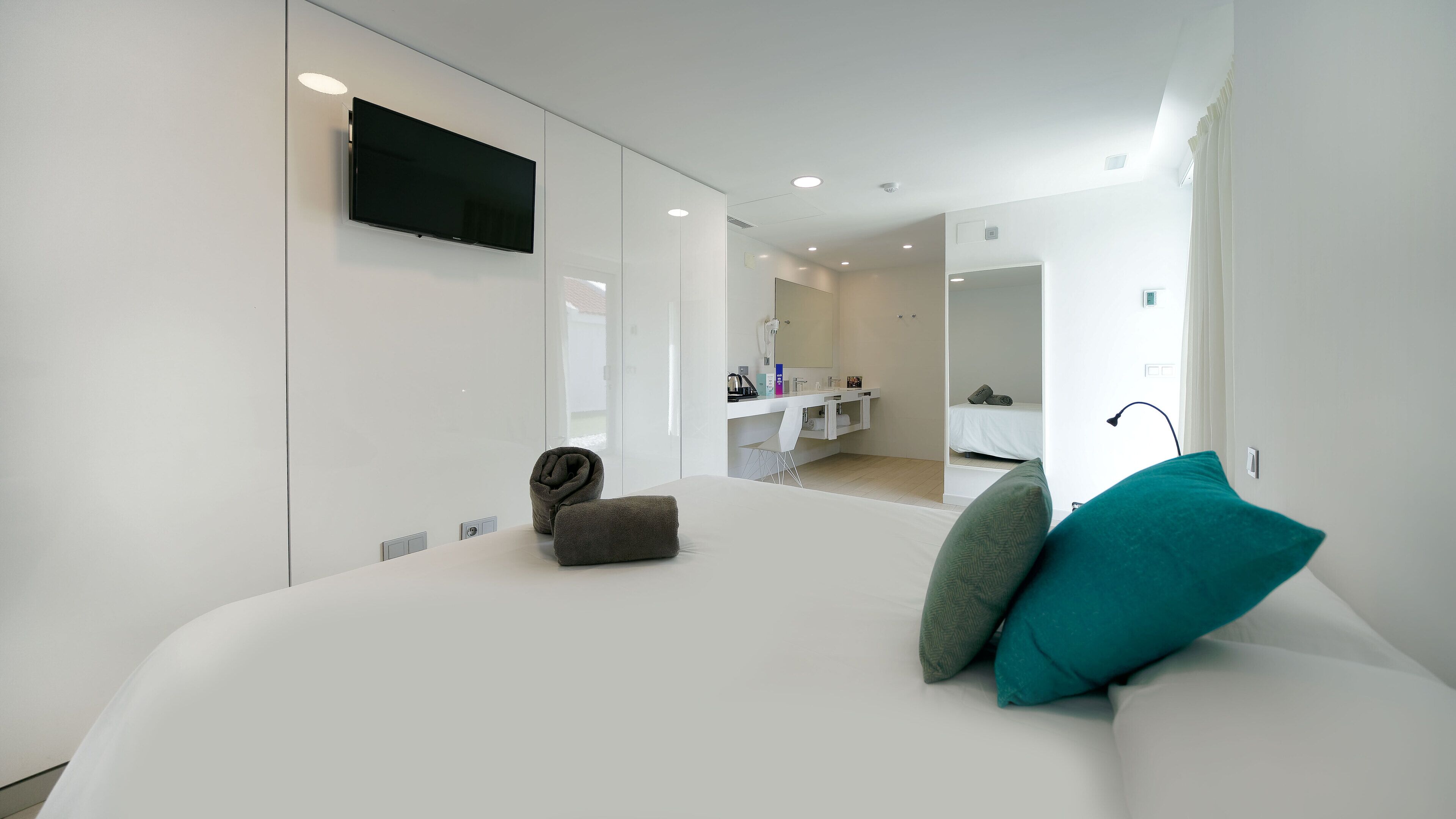 A modern hotel room with a large bed, a TV mounted on the wall, a walk-in closet, and a bathroom visible through an open door.
