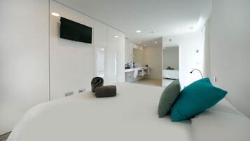 A modern hotel room with a large bed, a TV mounted on the wall, a walk-in closet, and a bathroom visible through an open door.