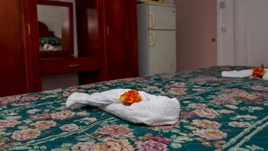 A bed with a floral bedspread, a white towel with a flower, and a microwave on a white cabinet. - Stephanie's Apartments Ltd (Gros Islet)