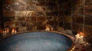 A stone-walled spa area with a blue-tiled hot tub, candles, and rose petals. - RVHotels Spa Vila de Caldes (Caldes de Montbui)