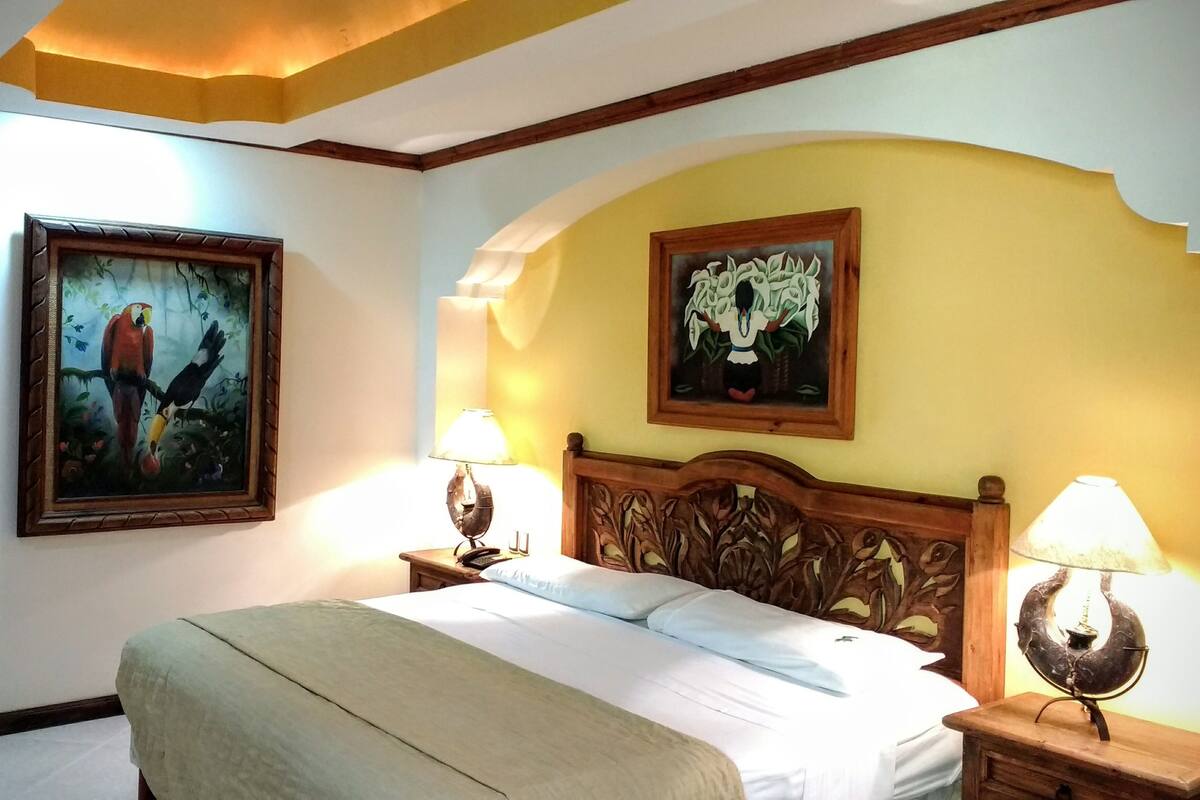 A hotel room with a bed, two bedside lamps, and two framed artworks on the walls.