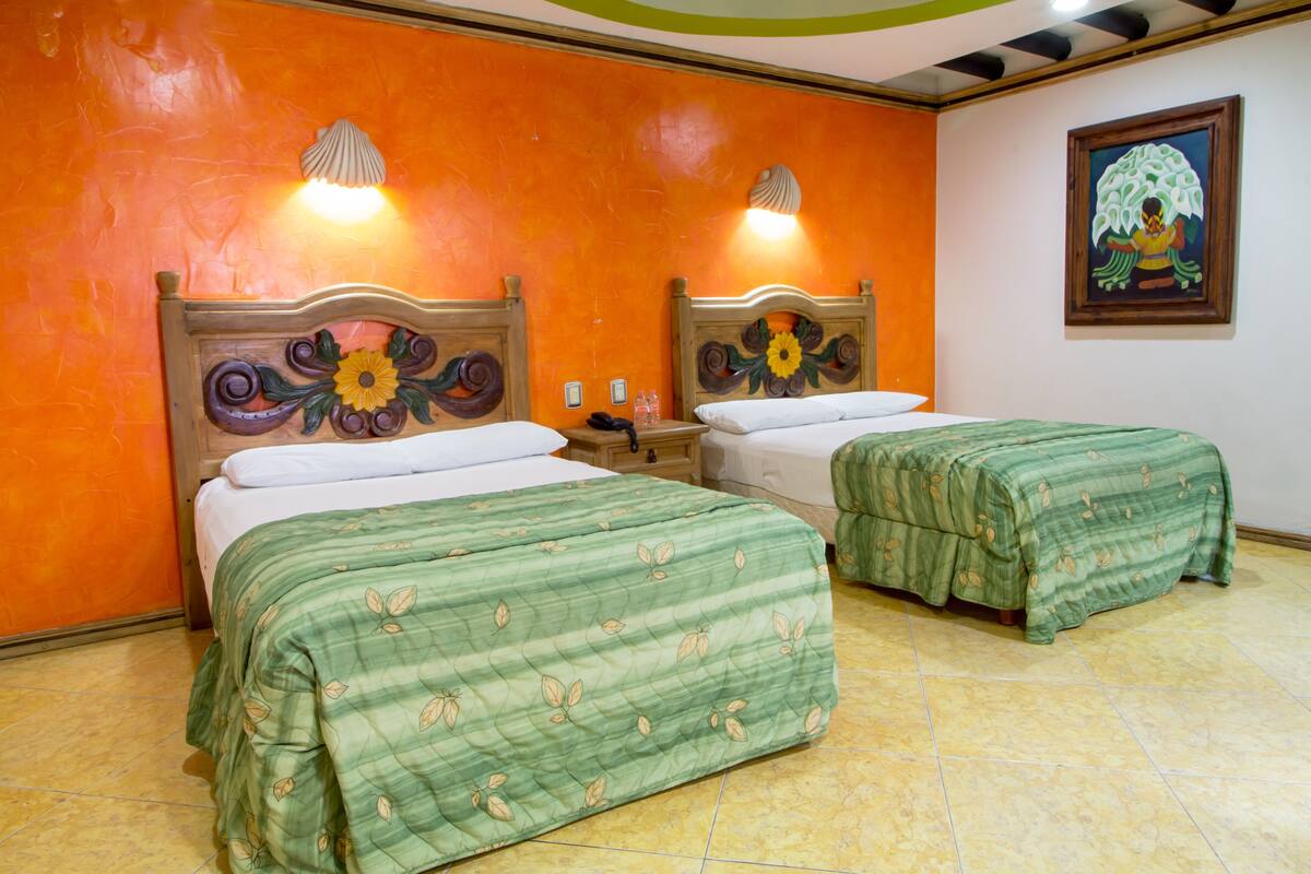 A hotel room with two beds, each with a floral headboard, a nightstand, and a wall-mounted light fixture.