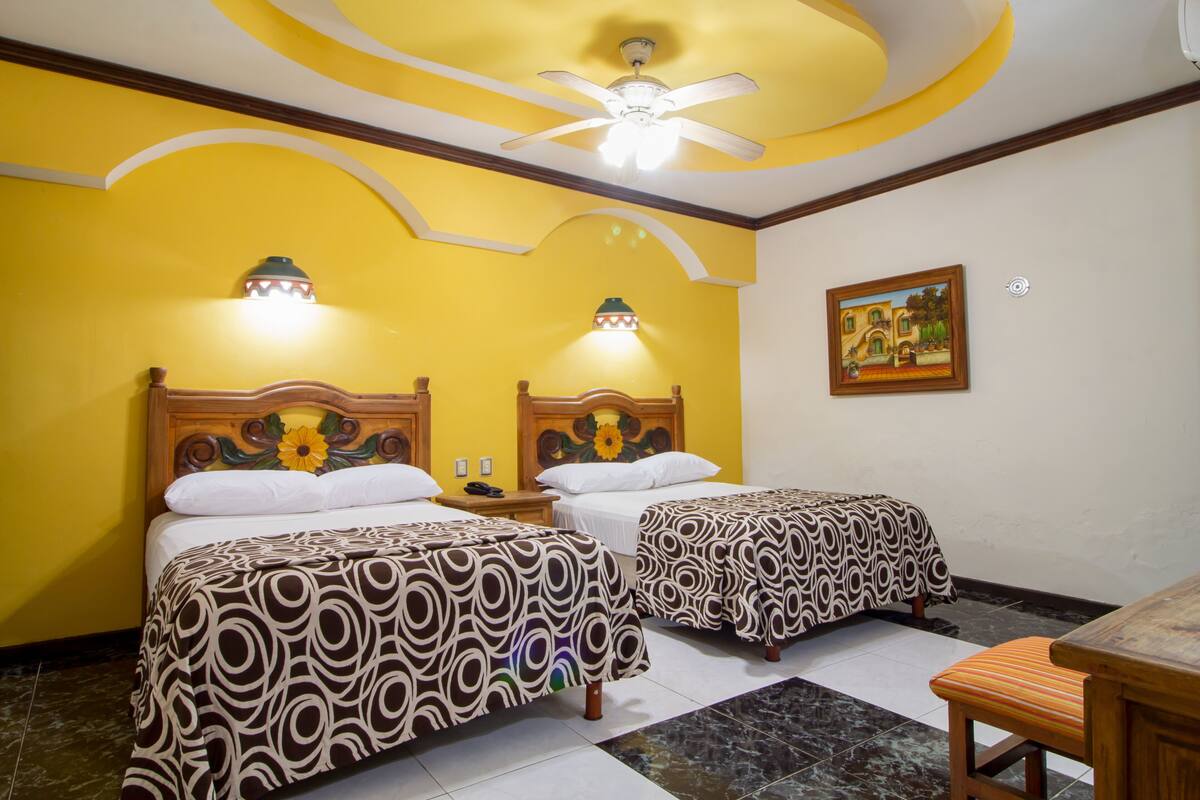 A hotel room with two beds, a ceiling fan, and a painting on the wall.