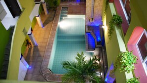 An indoor swimming pool with a tiled deck, surrounded by walls with plants and a seating area.