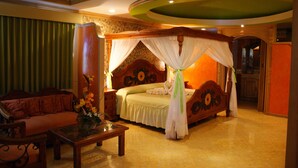 A spacious bedroom with a large bed, a sitting area with a sofa, and a small table with a vase.