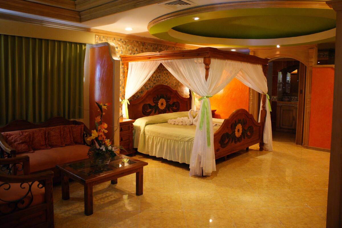 A spacious bedroom with a large bed, a sitting area with a sofa, and a small table with a vase.