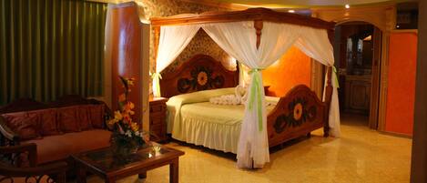 A spacious bedroom with a large bed, a sitting area with a sofa, and a small table with a vase.