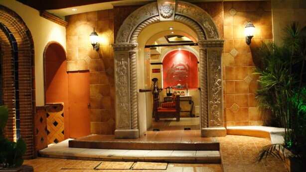 An entrance with a tiled archway, a red wall, and a staircase leading inside.