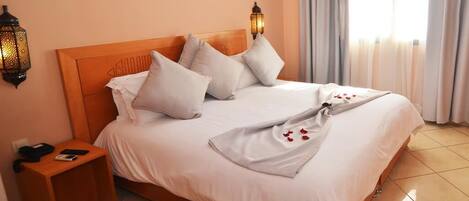 Una cama bien hecha con sábanas y almohadas blancas, un cabecero de madera y una mesita de noche con una lámpara.