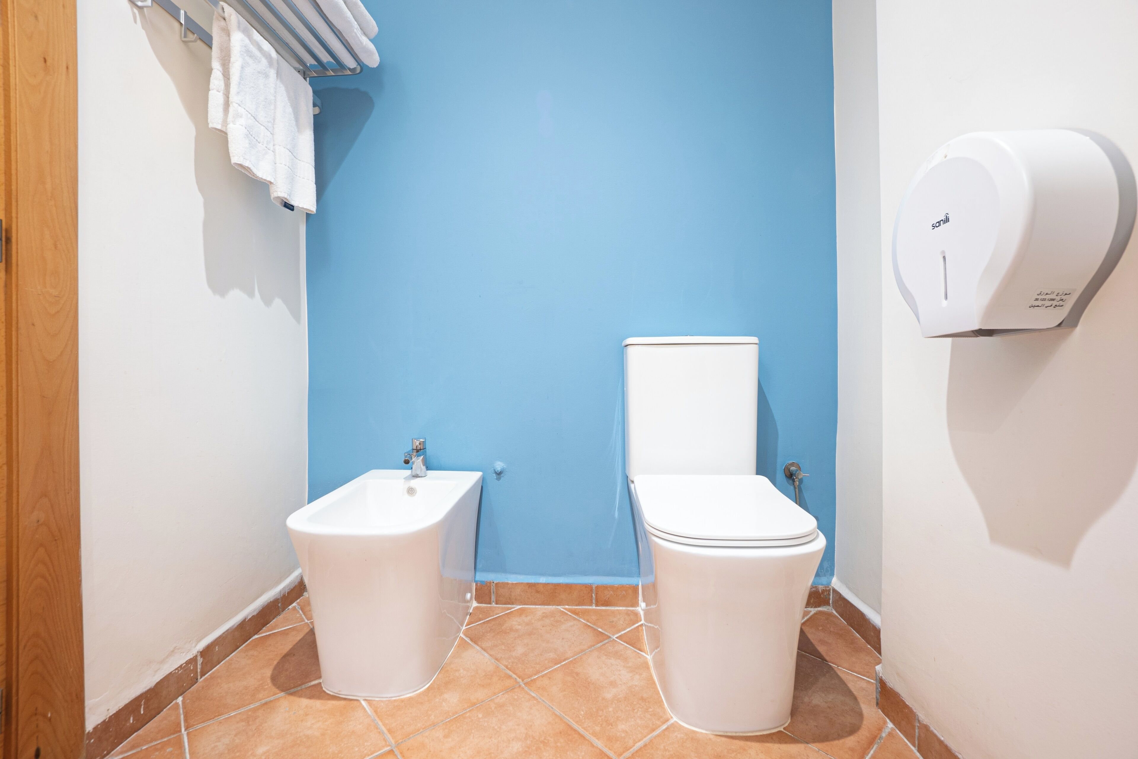 A bathroom with a blue wall, a white sink, a toilet, and a hand dryer.