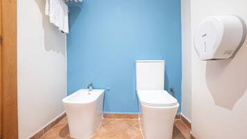 A bathroom with a blue wall, a white sink, a toilet, and a hand dryer.
