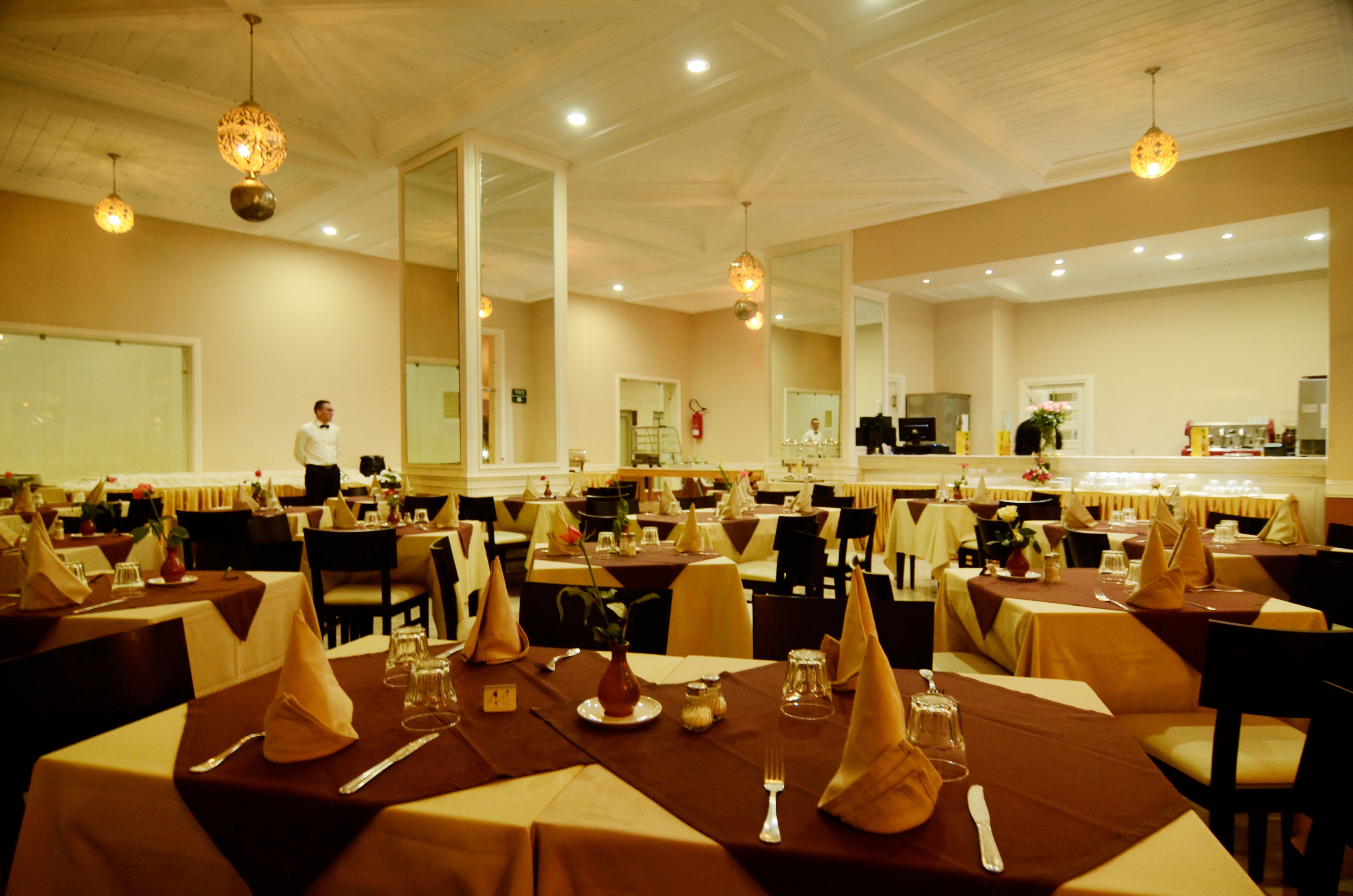 A banquet hall with multiple tables set for dining, a service area in the background, and a large mirror reflecting the room.
