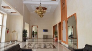 A spacious lobby with a high ceiling, a chandelier, a reception desk, and a large mirror.