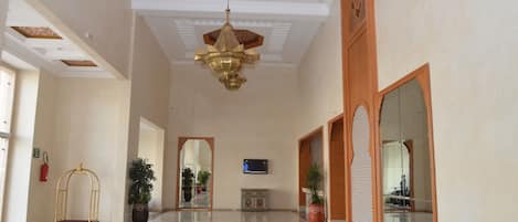 A spacious lobby with a high ceiling, a chandelier, a reception desk, and a large mirror.