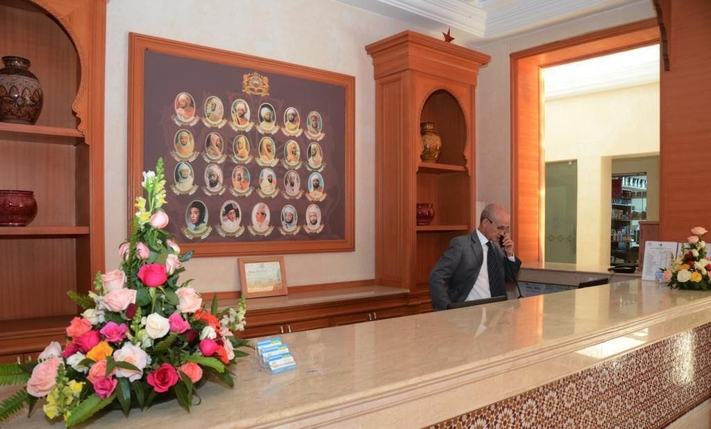 A reception area with a wooden reception desk, a wall-mounted portrait display, and a floral arrangement.