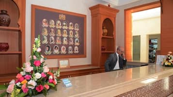 A reception area with a wooden reception desk, a wall-mounted portrait display, and a floral arrangement.