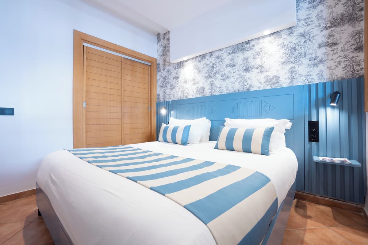 A hotel room with a large bed, a wooden door, a blue headboard, and a wall with a floral pattern.