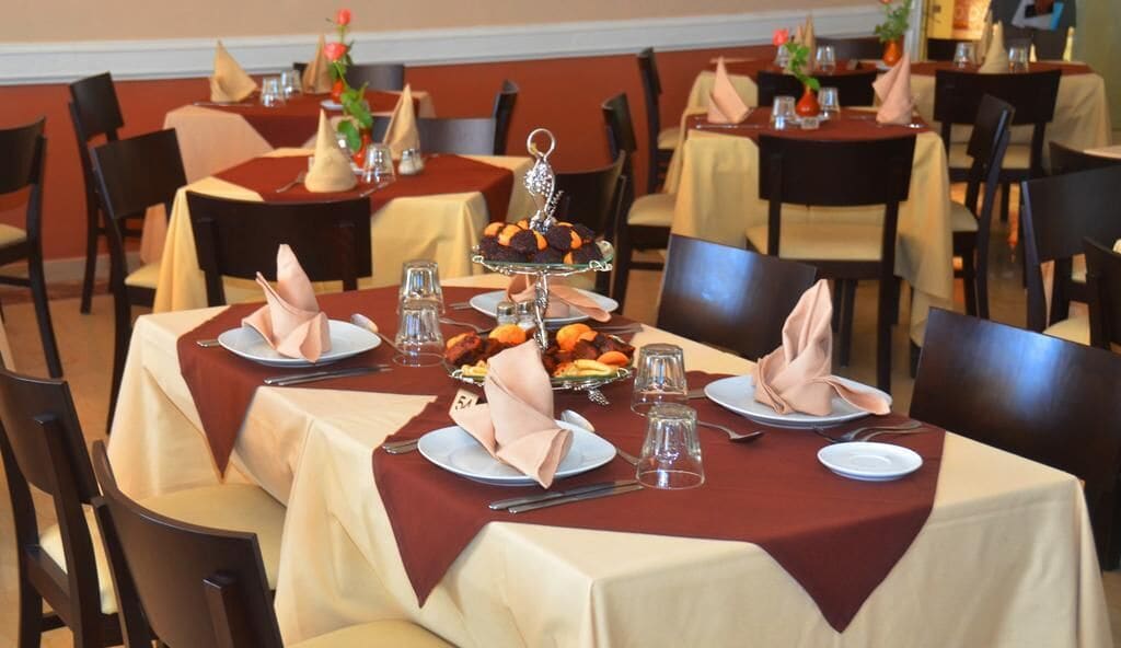 A dining area with tables set for four, each with a red tablecloth, white plates, and neatly folded napkins.