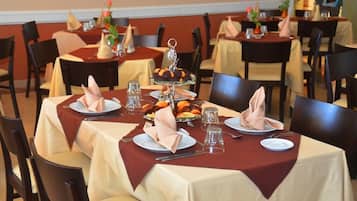 A dining area with tables set for four, each with a red tablecloth, white plates, and neatly folded napkins.
