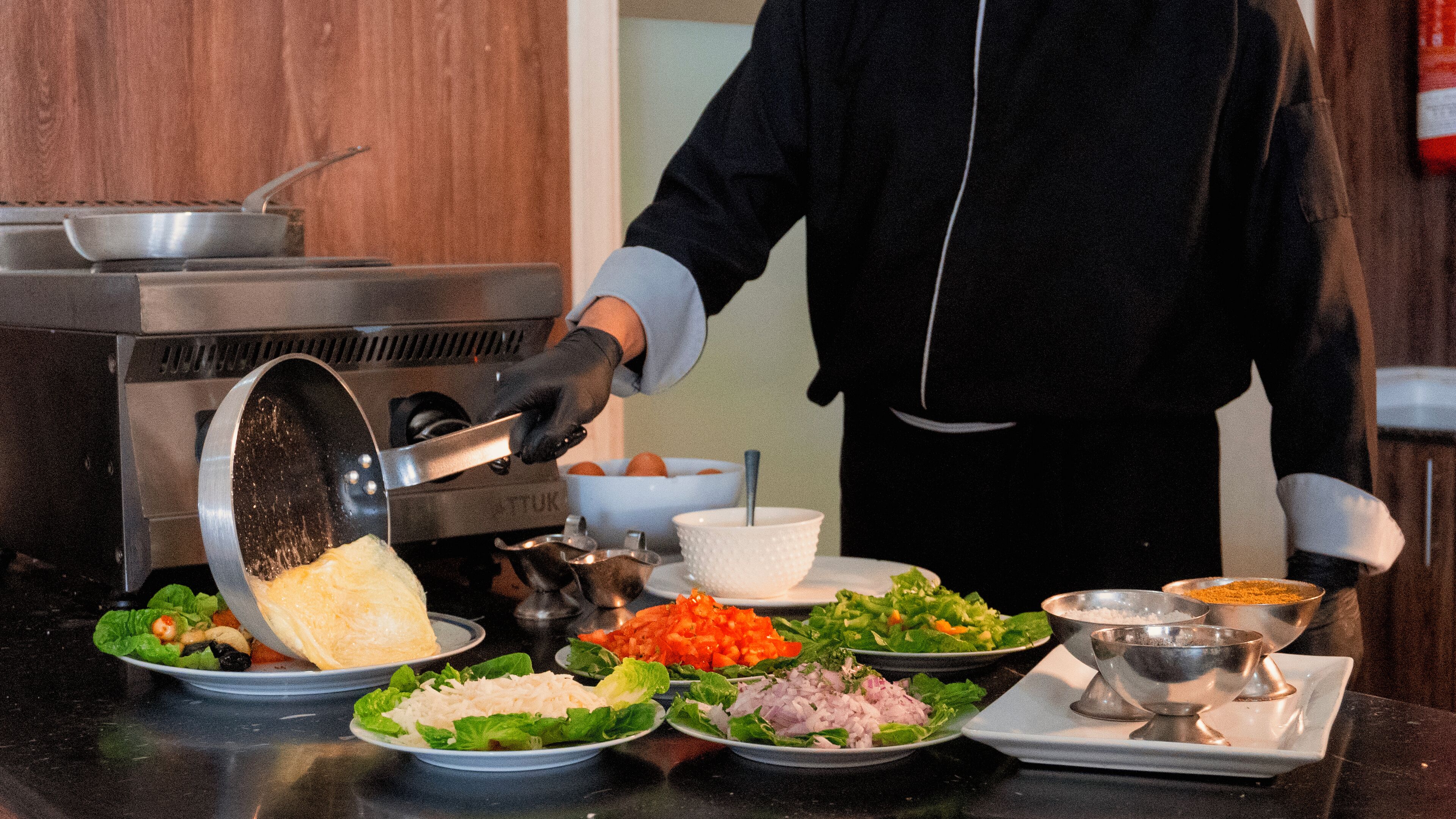 A person preparing food with a pan on a stove, surrounded by various dishes and ingredients.