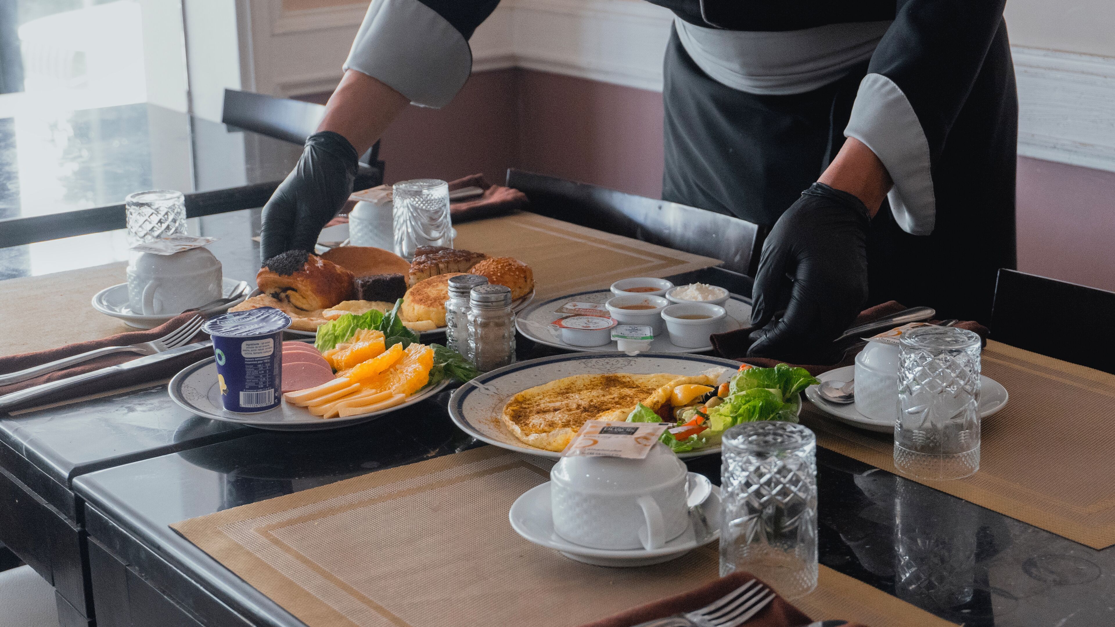 A breakfast setting with plates of food, cups, and cutlery on a table.