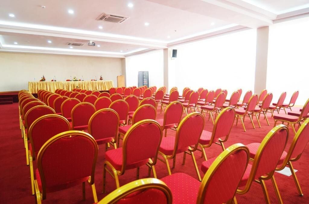 Un salón de conferencias con filas de sillas rojas y un atril al frente.