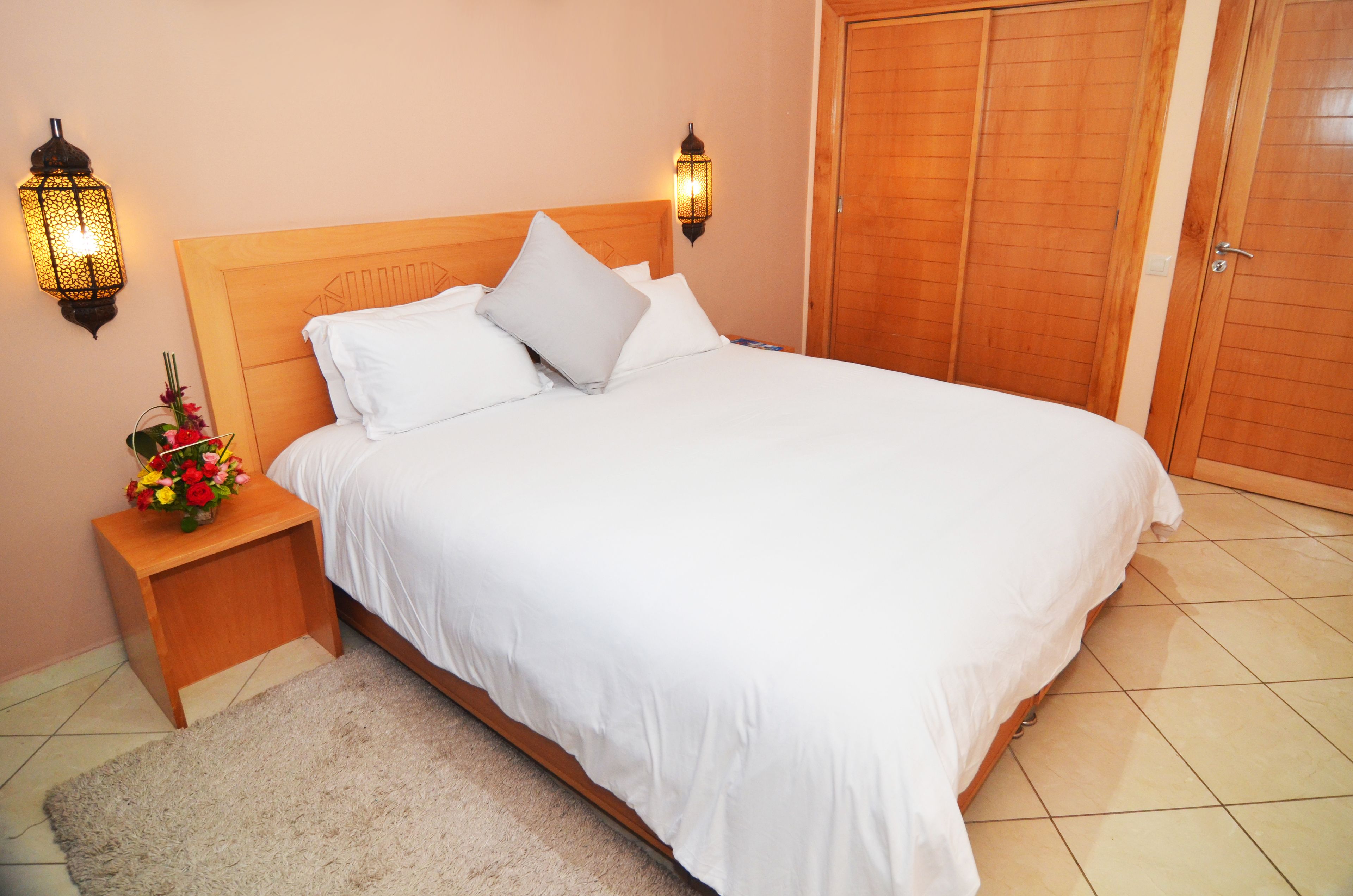Una cama bien tendida con ropa blanca, cabecera de madera y dos lámparas fijadas a la pared.