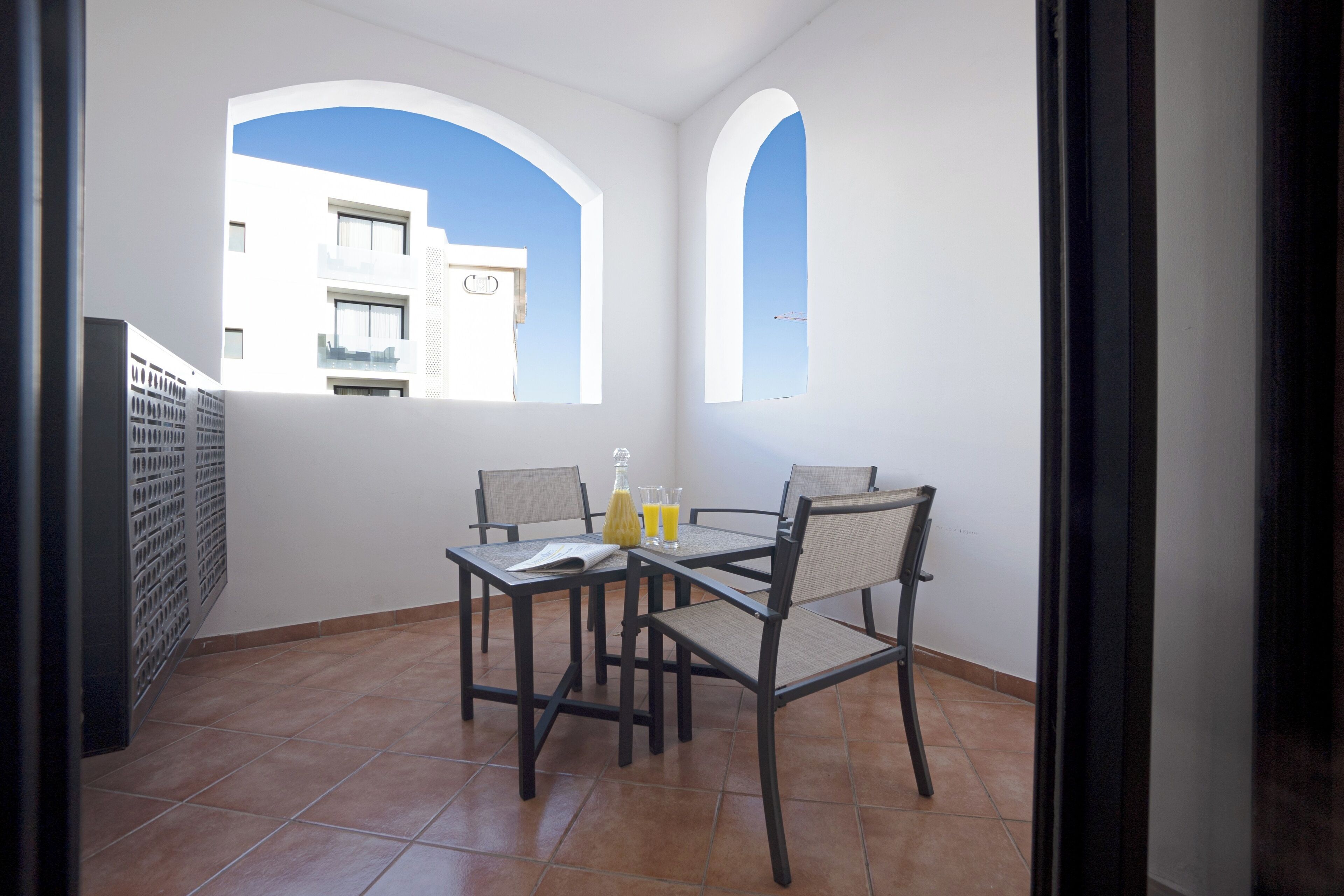 A balcony with a table and chairs, a view of a building, and a tiled floor.