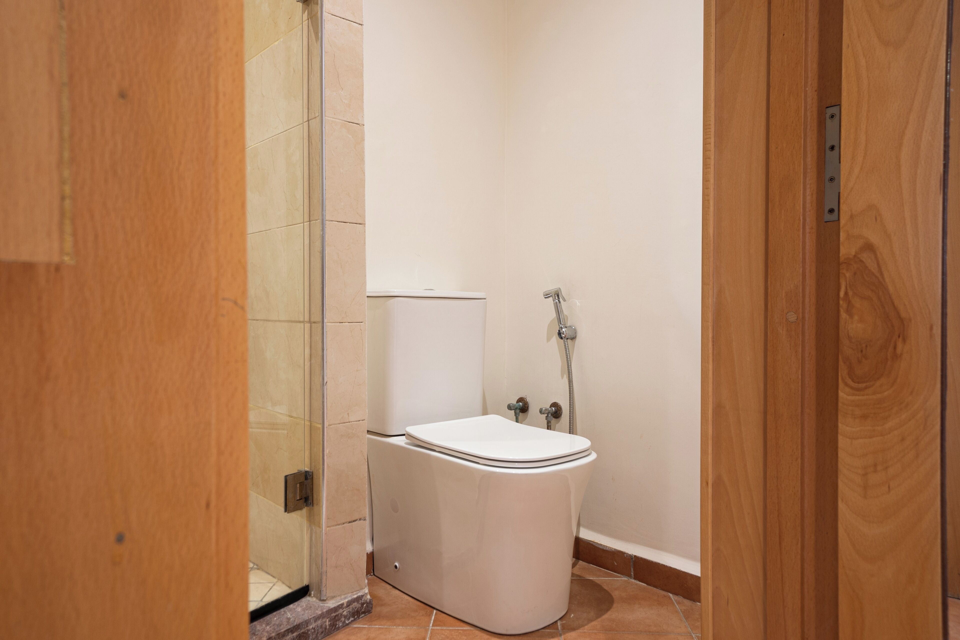 A compact bathroom with a toilet, shower, and a wooden door.