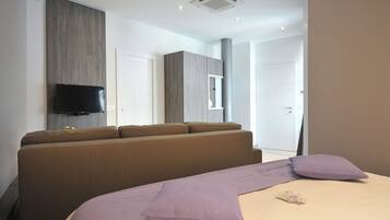 Habitación de hotel moderna con una cama grande, un sofá, un televisor de pantalla plana montado en la pared y un amplio ventanal.