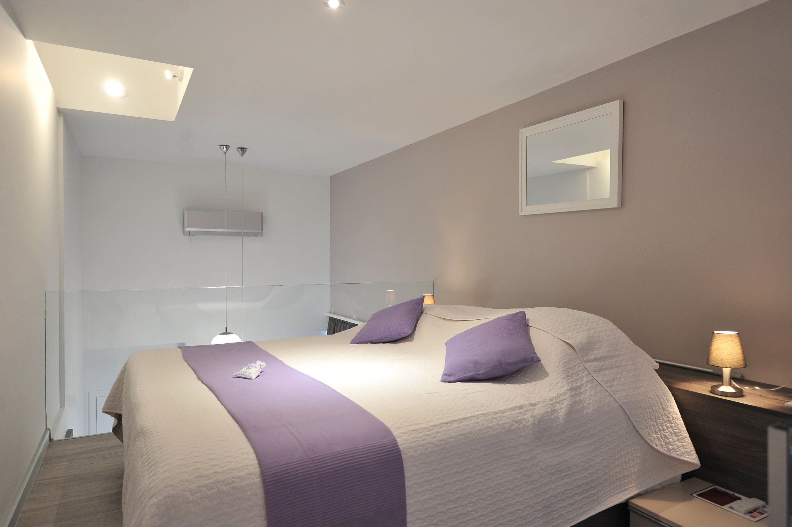 Une chambre d’hôtel moderne avec un grand lit, une table de chevet avec une lampe, un miroir au mur et un luminaire au plafond.