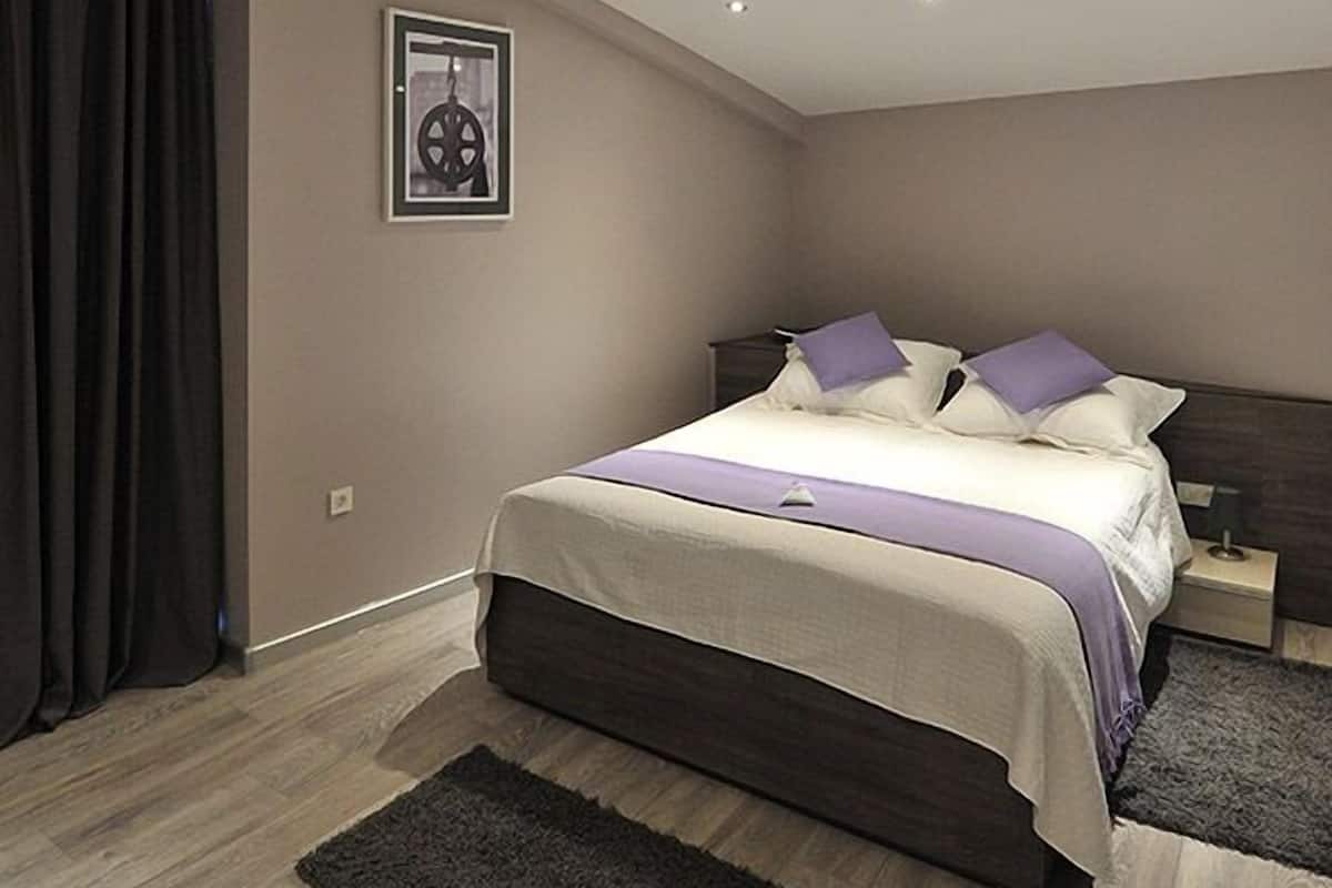 A modern bedroom with a bed, a ceiling vent, a framed picture, and a dark rug.
