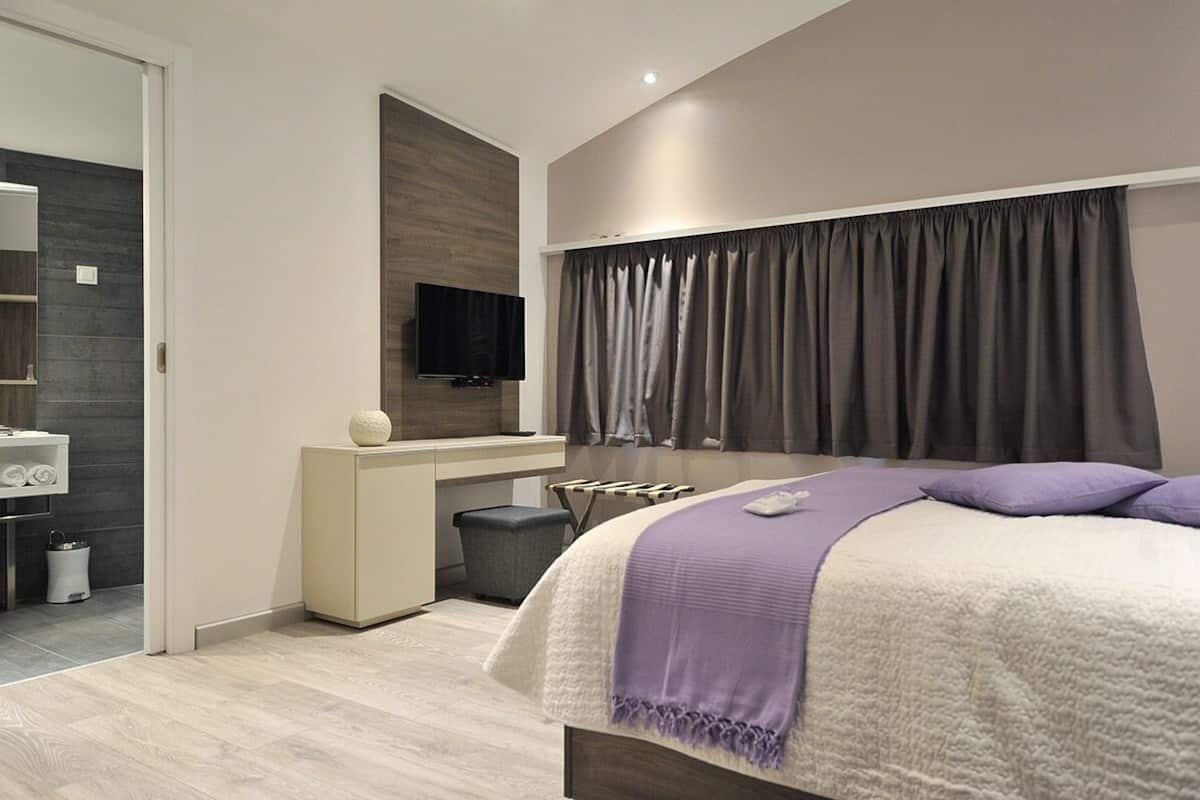 A modern bedroom with a bed, a desk, a television, and a large window with curtains.