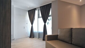 Ein modernes Wohnzimmer mit einer Couch, einem Couchtisch und großen Fenstern mit Vorhängen.