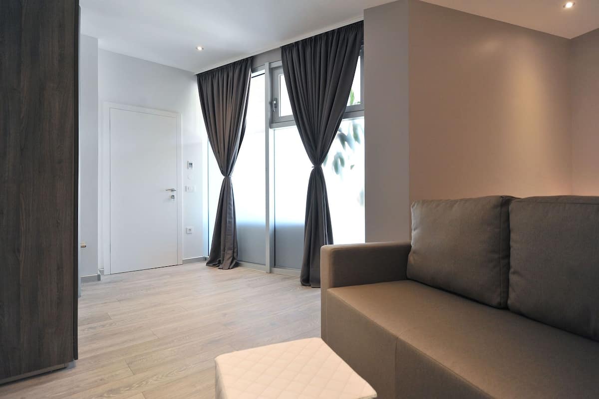 A modern living room with a sofa, a coffee table, and large windows with curtains.