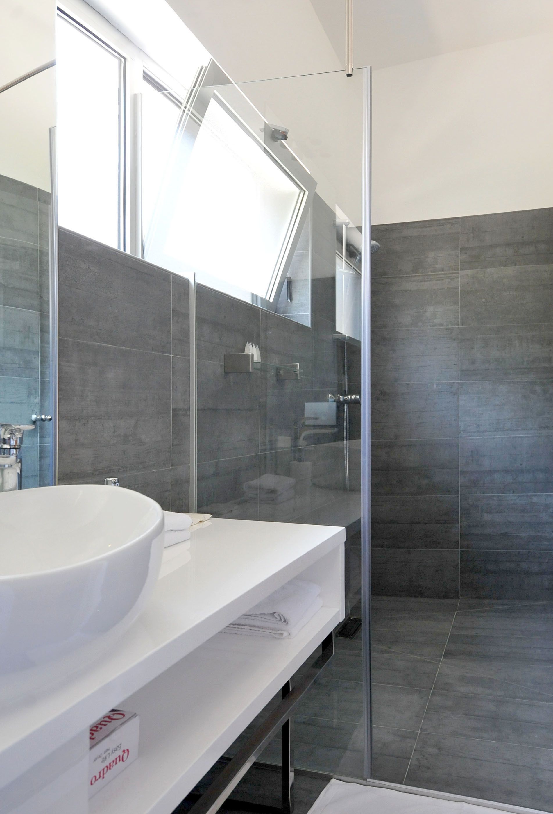 A modern bathroom with a large white sink, a glass shower enclosure, and a large mirror.