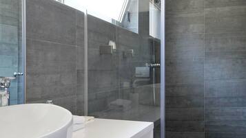 A modern bathroom with a large white sink, a glass shower enclosure, and a large mirror.