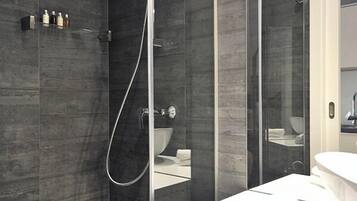 A modern bathroom with a glass-enclosed shower, a white vanity with a mirror, and neatly rolled towels.