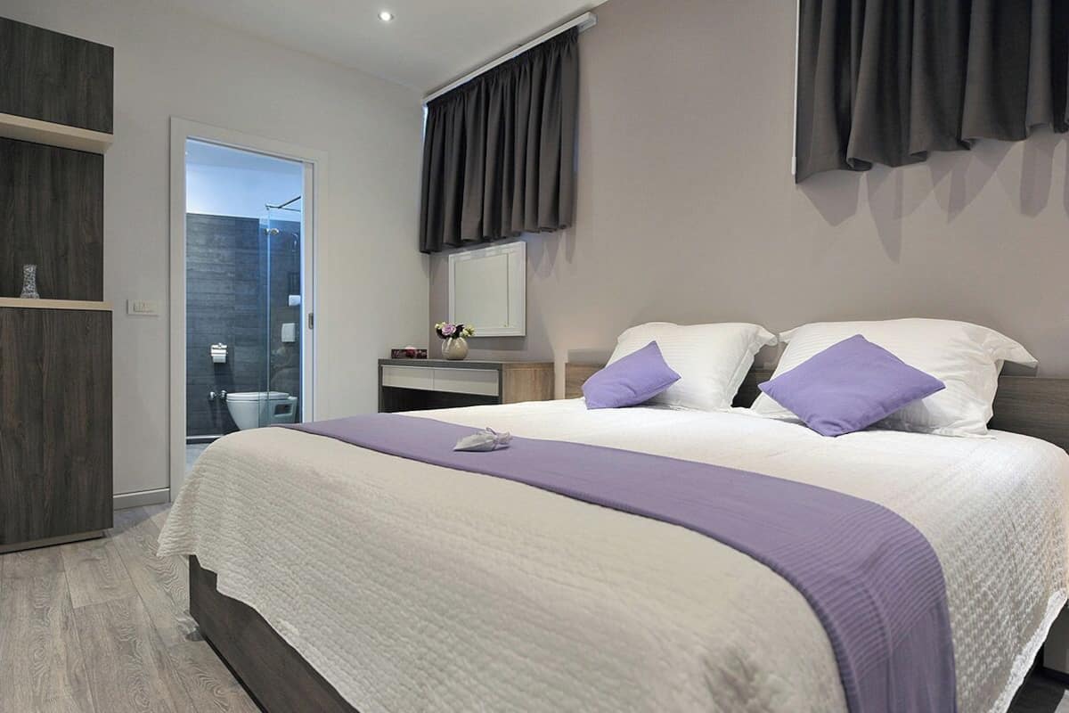 A modern bedroom with a large bed, a bedside table, a mirror, and a wardrobe.
