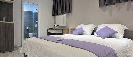 A modern bedroom with a large bed, a bedside table, a mirror, and a wardrobe.