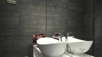 Un baño moderno con paredes de azulejos oscuros, un lavamanos grande de color blanco y un espejo sobre el mueble de tocador.