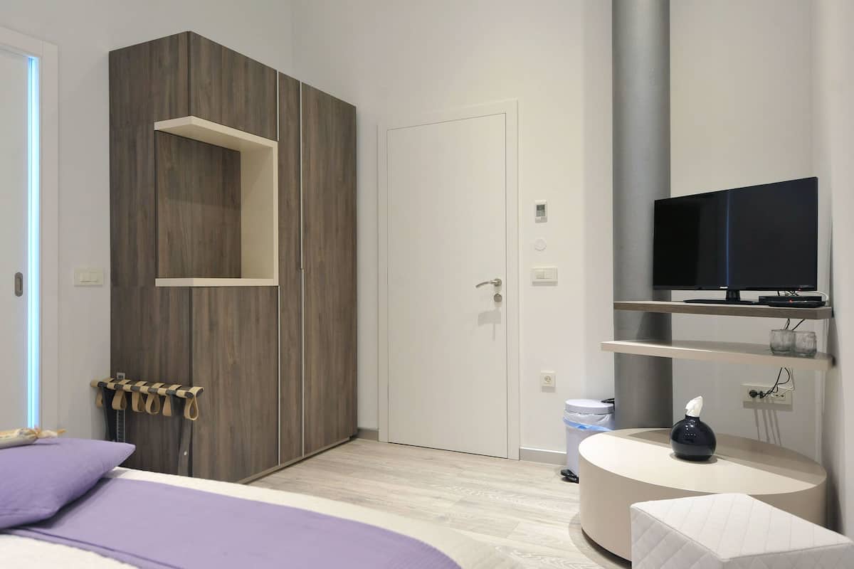 A modern bedroom with a bed, a wardrobe, a television, and a small table.