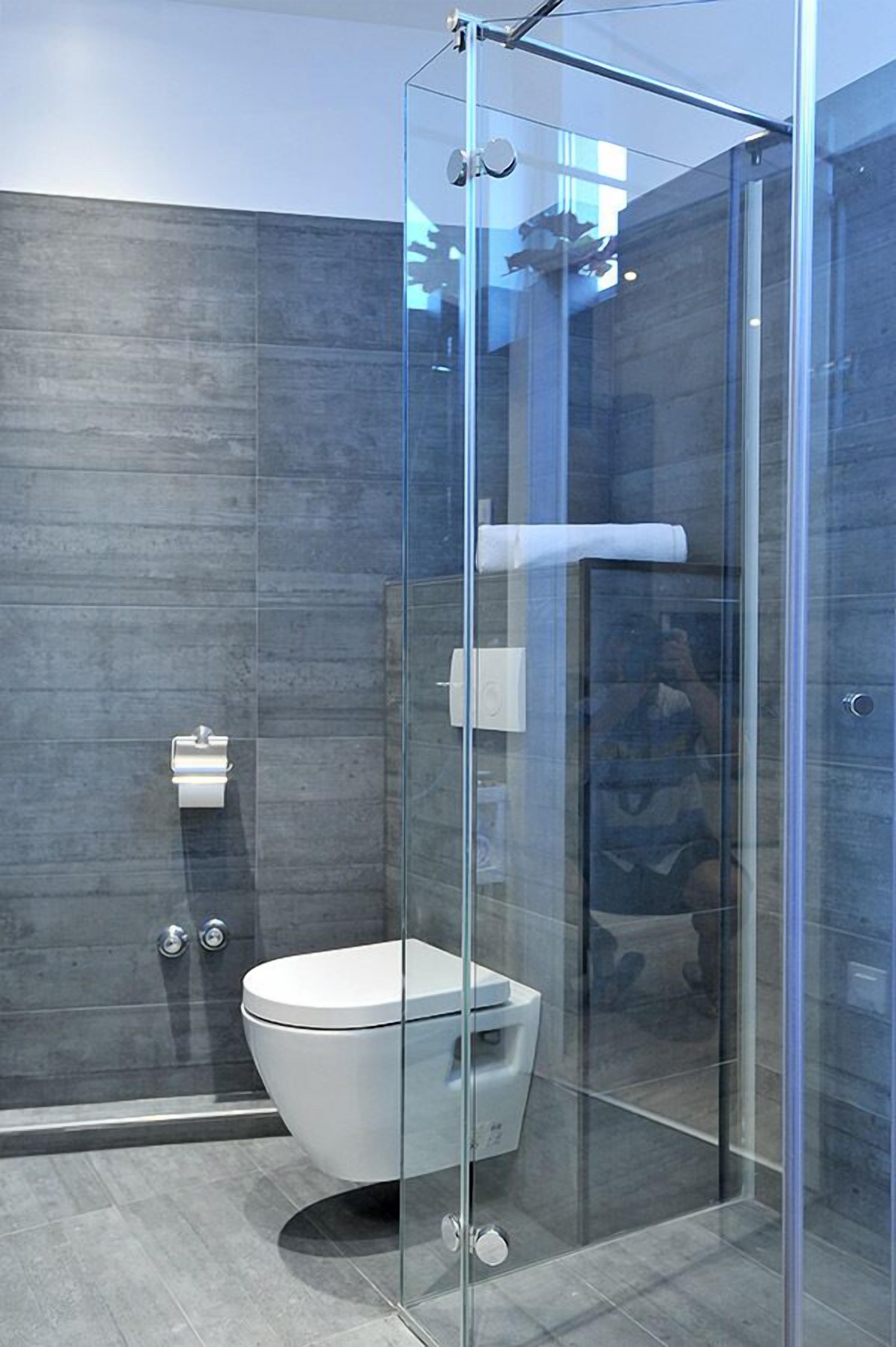 A modern bathroom with a glass-enclosed shower, a white toilet, and a towel dispenser.