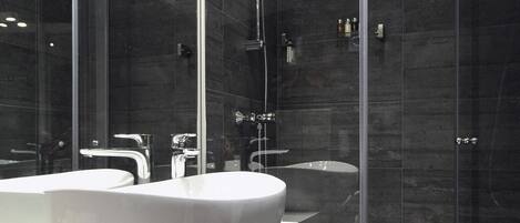A modern bathroom with a large white sink, a glass-enclosed shower, and dark tiled walls.